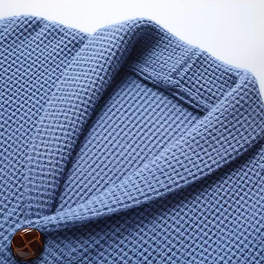 Blue knitted cardigan with a close-up of the collar and sleeve on a light gray background.