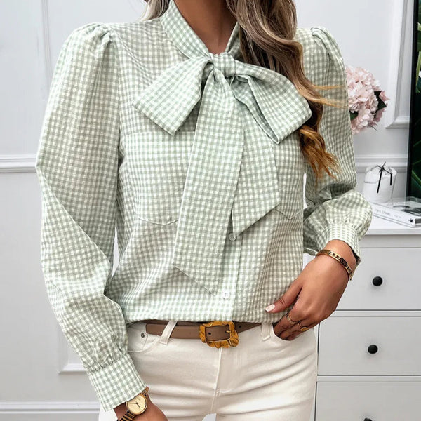 Person wearing a green checkered blouse with a bow tie in an indoor setting.