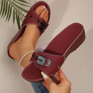 Maroon slide sandals with a buckle held by a hand against a neutral background