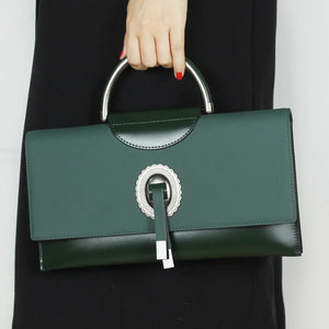 Green handbag with silver handle and clasp held by a person wearing a black coat.