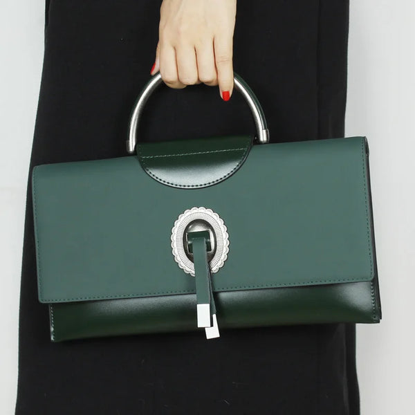 Green handbag with silver handle and clasp held by a person wearing a black coat.