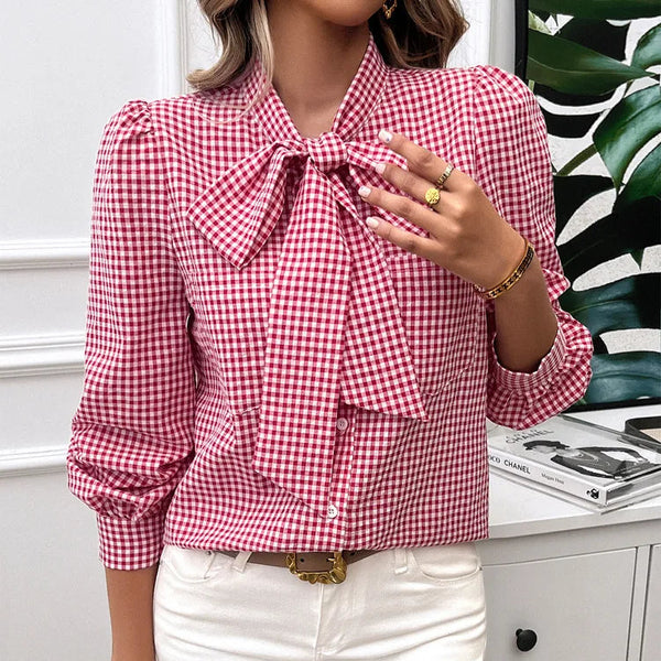 Person wearing a red and white checkered blouse with a bow tie, white pants, and holding a small white handbag.