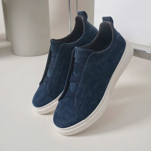 Pair of navy blue slip-on sneakers on a white surface with a neutral background