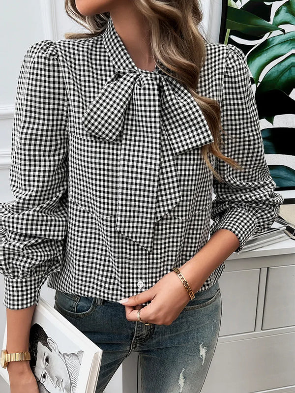 Person wearing a black and white checkered blouse with a bow detail, standing against a light-colored wall.