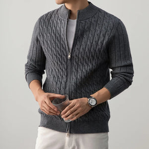 Person wearing a gray cable knit sweater with a plain background