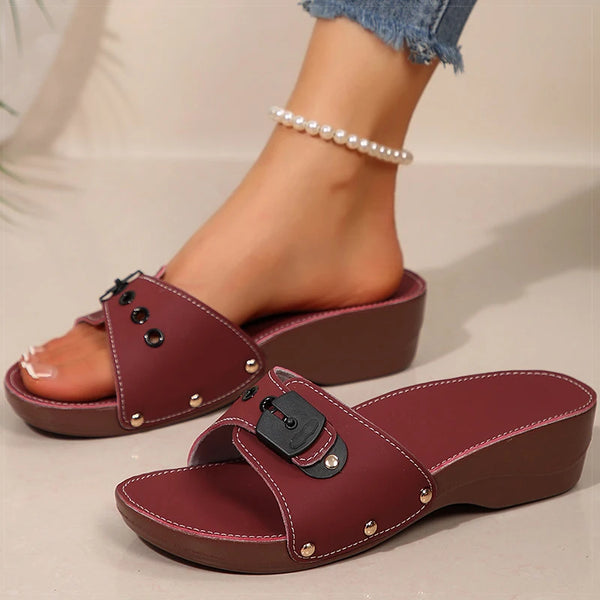 Maroon sandals with black buckles worn by a person on a neutral background