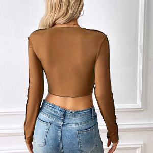 Person wearing a brown sheer long-sleeve top and blue jeans against a white wall.