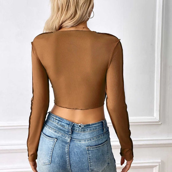 Person wearing a brown sheer long-sleeve top and blue jeans against a white wall.