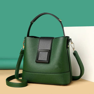 Green handbag with a black flap on a beige surface with a teal background
