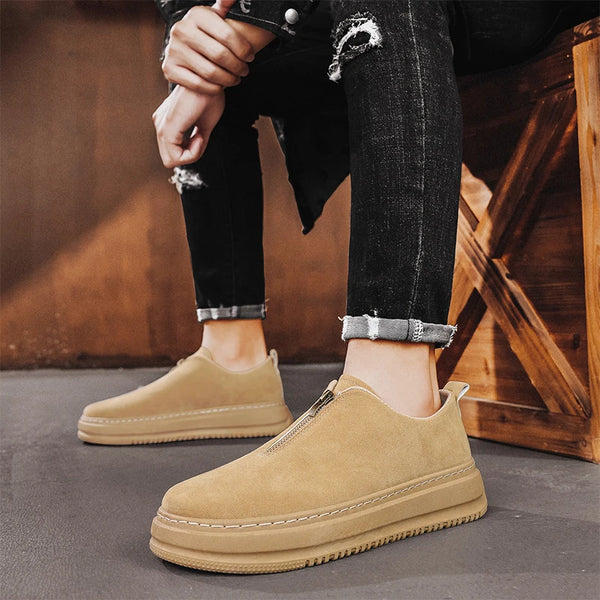 Beige slip-on shoes worn with black jeans against a wooden background