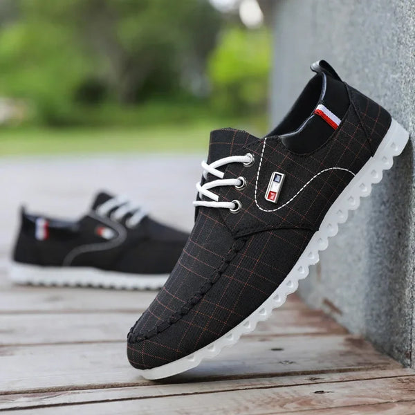 Black casual shoes with white soles on a wooden surface.