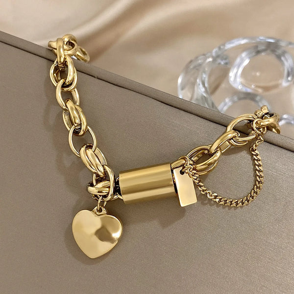 Gold bracelet with heart charm and cylindrical clasp on a beige surface