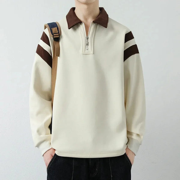 Person wearing a cream-colored sweater with brown accents on a plain background