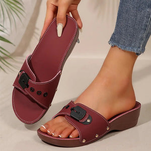 Maroon sandals with black buckles worn by a person on a neutral background