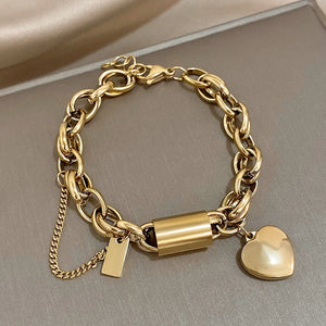 Gold chain bracelet with a lock and heart charm on a neutral background