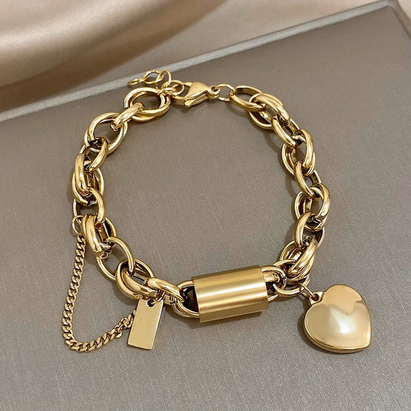 Gold chain bracelet with a lock and heart charm on a neutral background