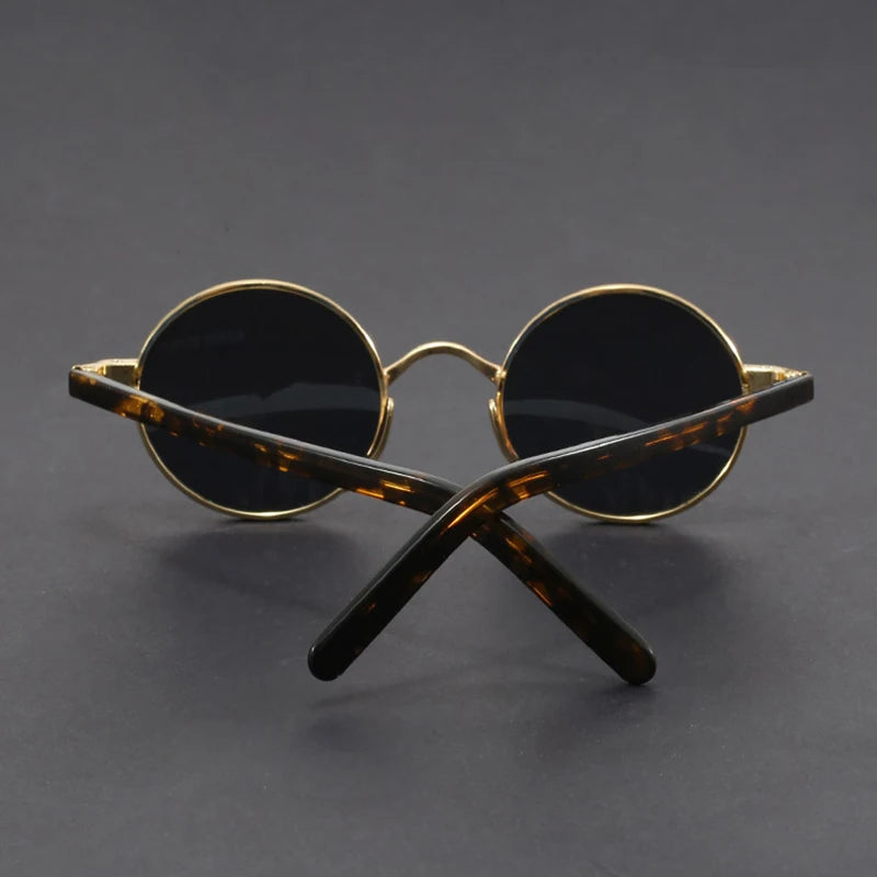 Round sunglasses with gold frame and black lenses on a dark gray background