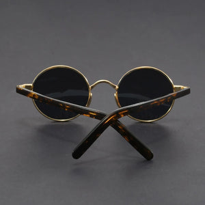 Round sunglasses with gold frame and black lenses on a dark gray background