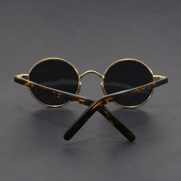 Round sunglasses with gold frame and black lenses on a dark gray background