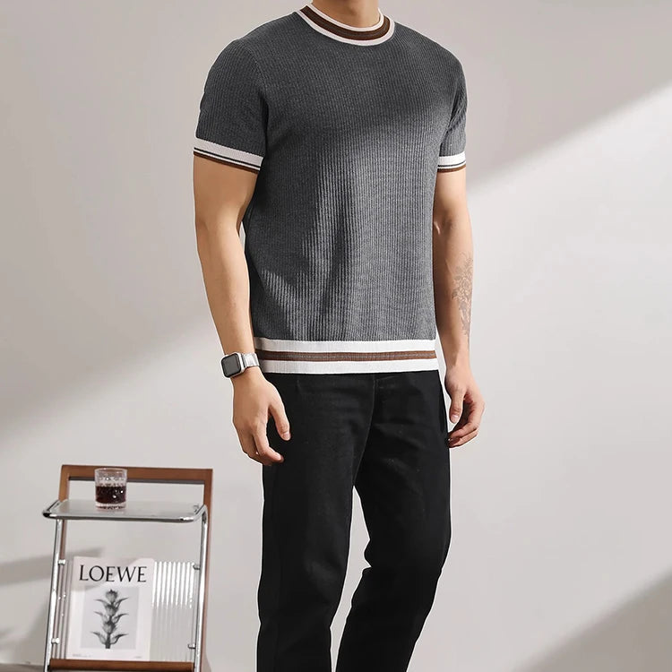 Person wearing a gray short-sleeve sweater with white stripes and black pants, standing against a plain background.