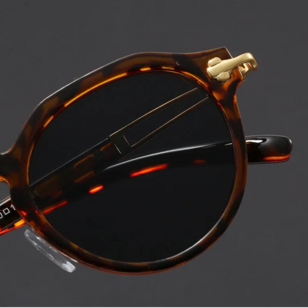 Close-up of a tortoiseshell sunglasses with gold accents on a dark background