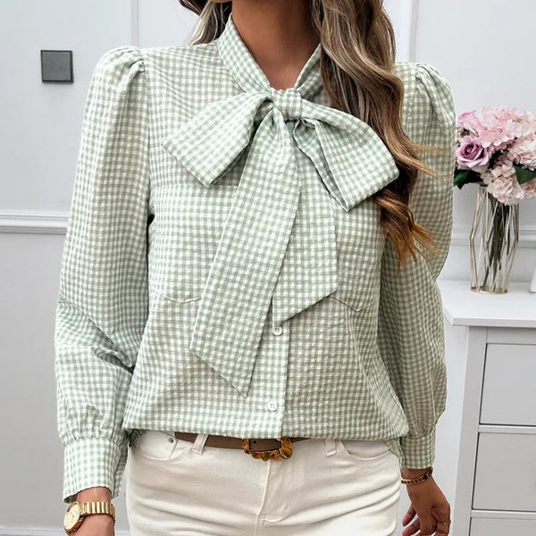 Person wearing a green checkered blouse with a large bow tie in a room. 