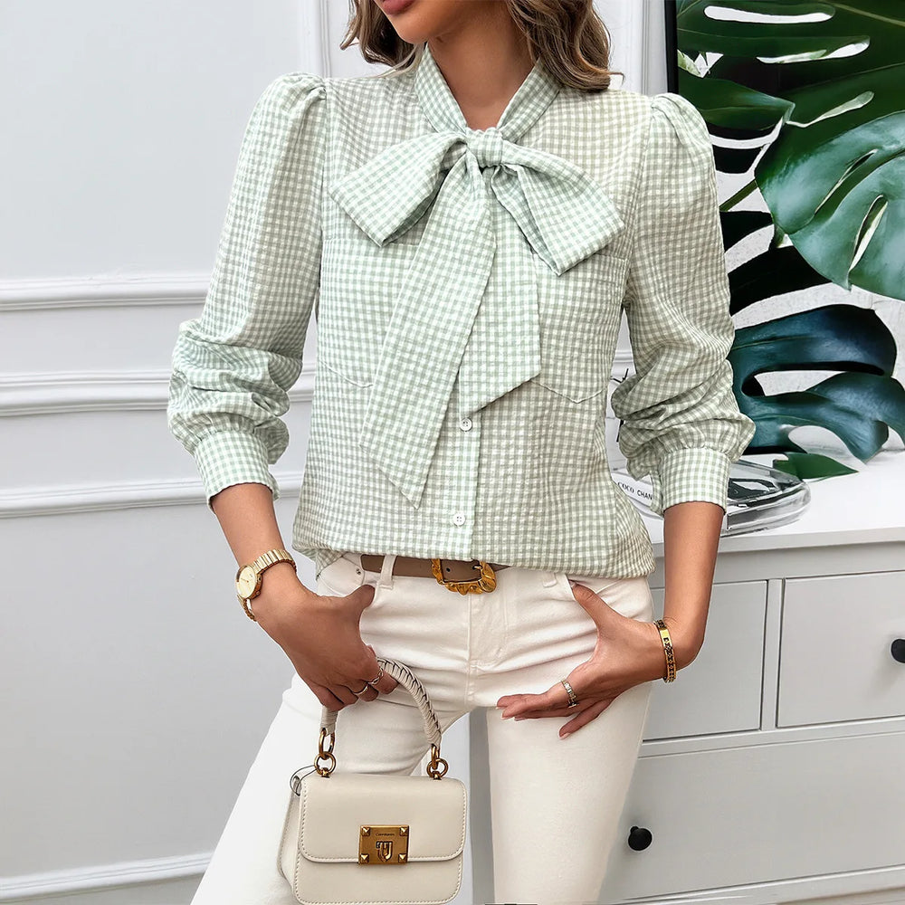 Woman wearing a green checkered blouse with a bow tie, holding a beige handbag.