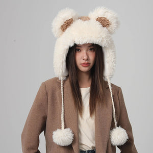 Person wearing a fluffy bear-themed hat with pom-poms on a gray background