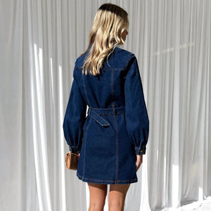 Woman wearing a blue denim dress against a white curtain background