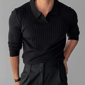 Person wearing a black ribbed sweater over a collared shirt with dark pants on a gray background