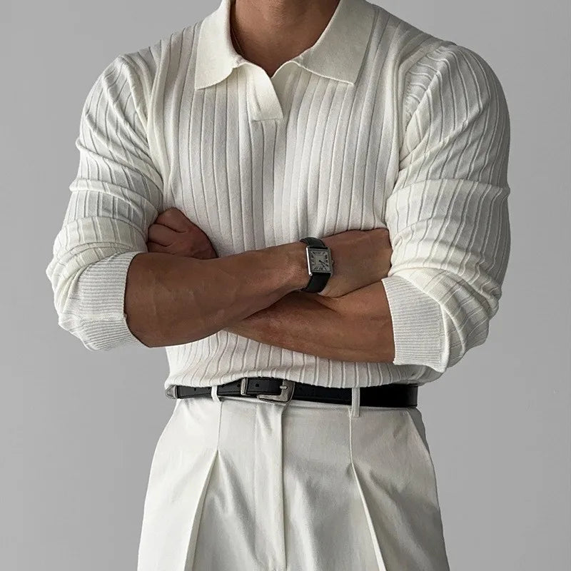 Person wearing a white ribbed sweater and light-colored pants with arms crossed on a gray background