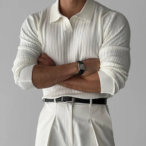 Person wearing a white ribbed sweater and light-colored pants with arms crossed on a gray background