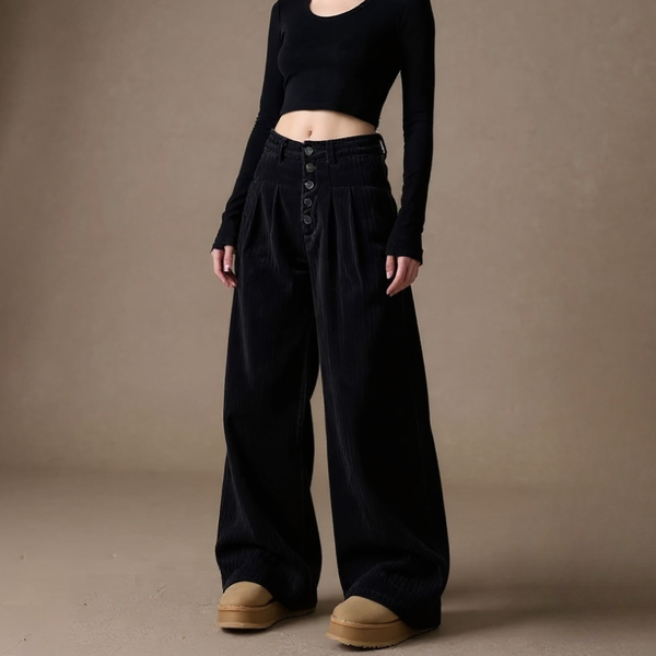 Person wearing a black outfit with wide-leg pants on a brown background