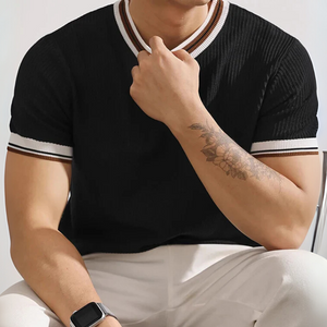 Person wearing a black short-sleeve shirt with white trim, sitting against a neutral background.