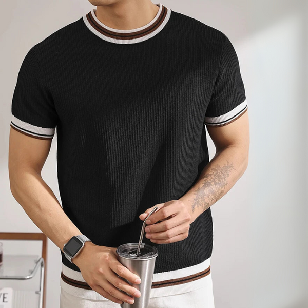 Person wearing a black ribbed sweater with white and brown trim, holding a silver tumbler.