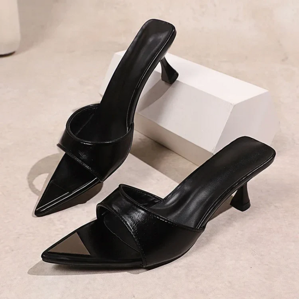 Black high-heeled shoes on a beige surface with a white box in the background