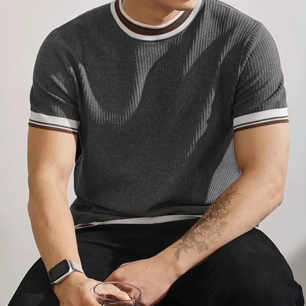 Person wearing a dark gray knit shirt with white trim, sitting against a plain background.