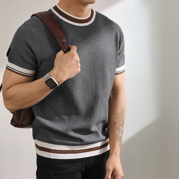 Person wearing a gray ribbed sweater with white and brown trim, holding a brown bag.